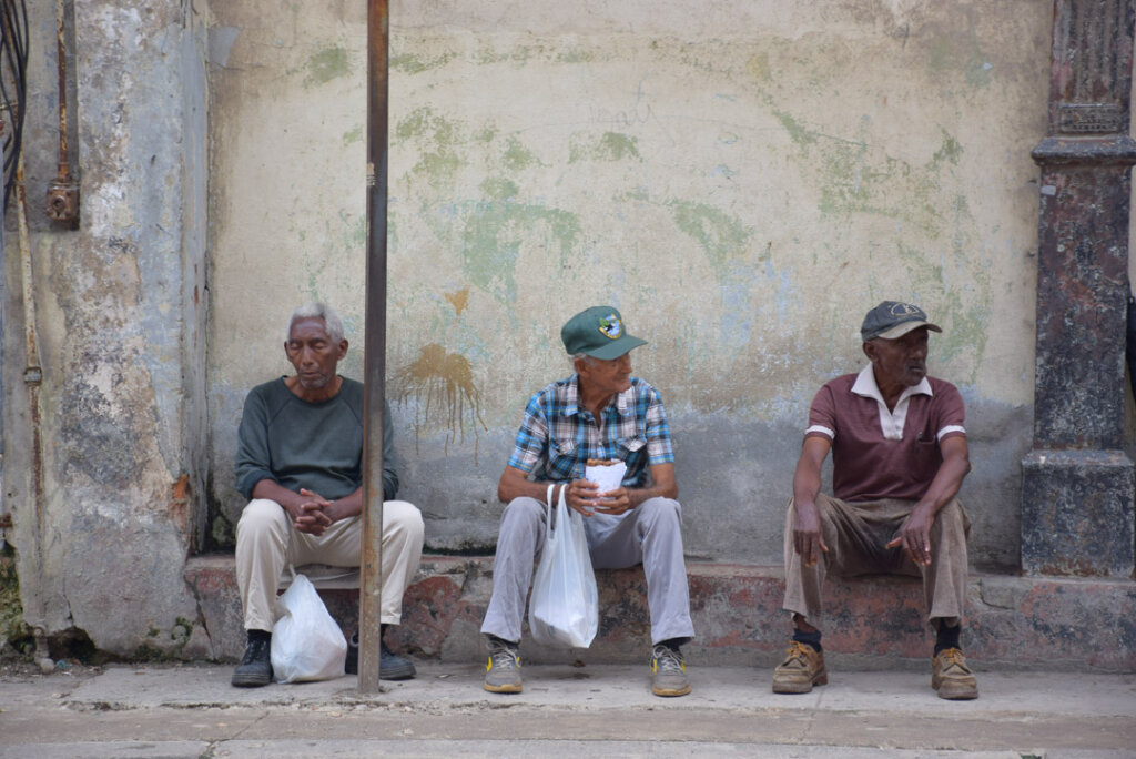 three old Cuban men sit of a step in the city