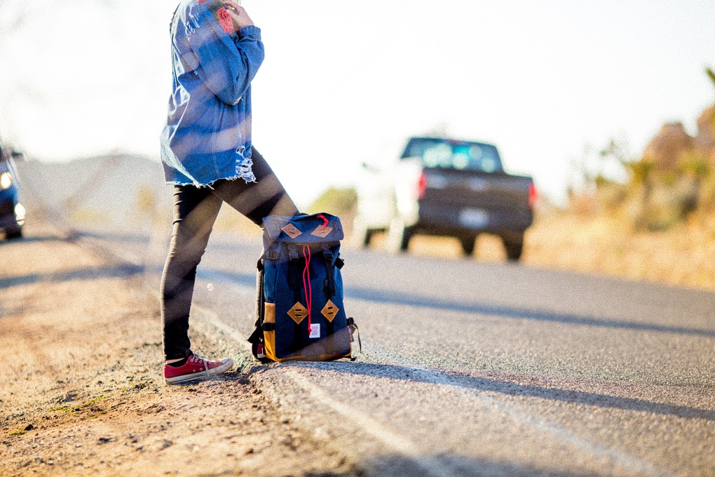 girl hitchhiking with backpack on the side of the road