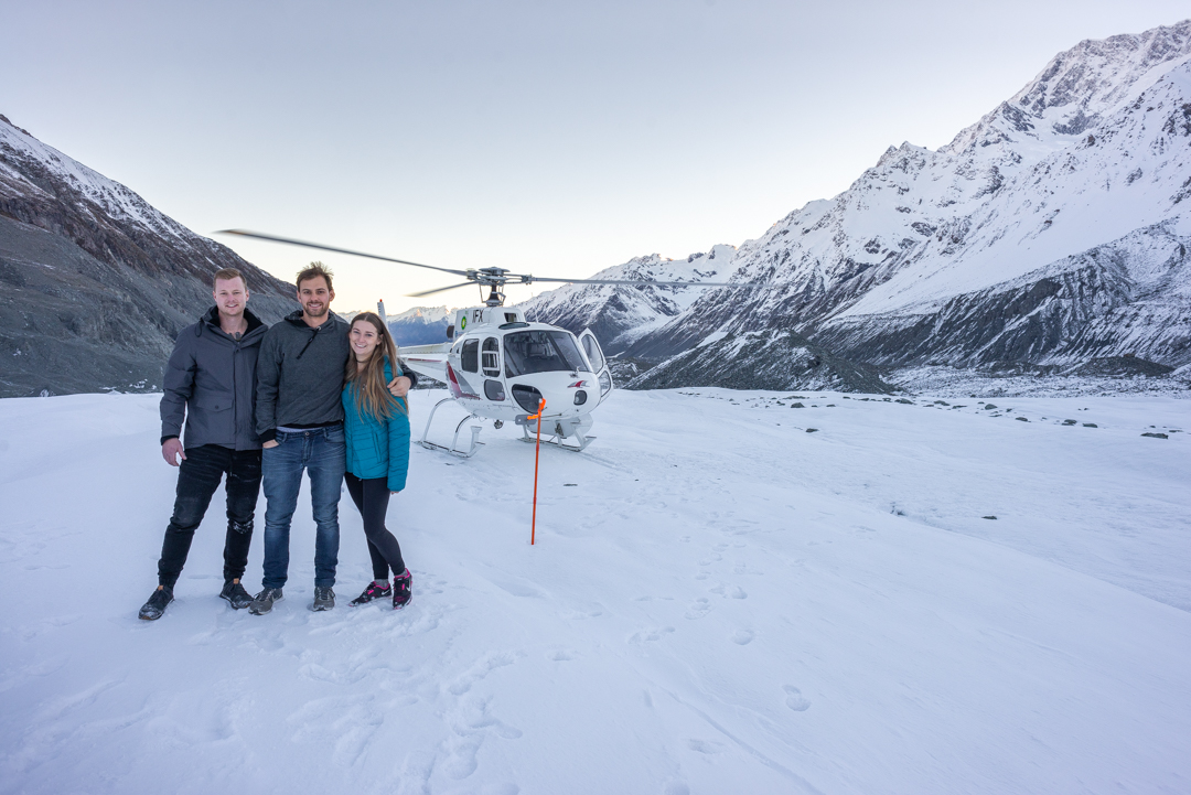 three poepl stand on the Hooker Glacier next to a helicopter in Mount Cook National Park