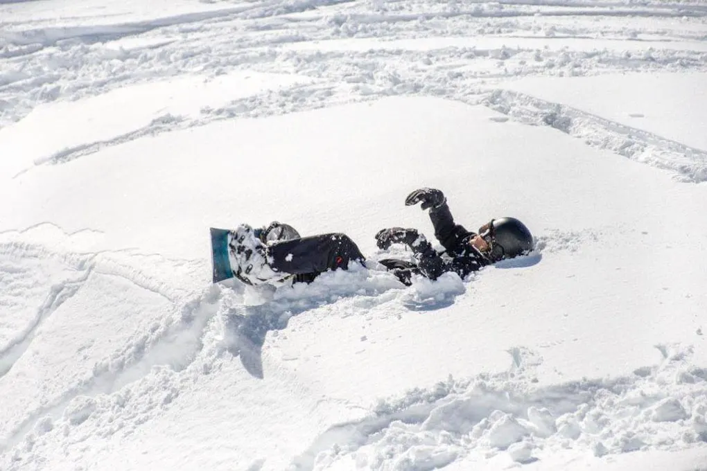 A man sits in the snow with his snowboard