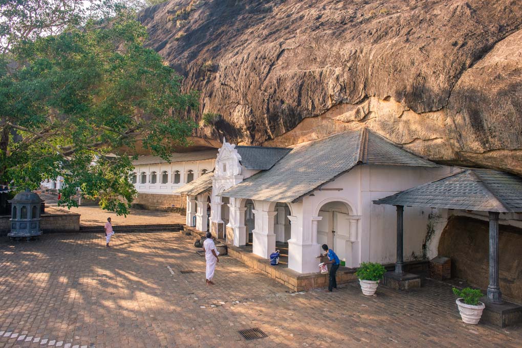 person praying outside of the entrance to the Dambulla Cave Temples