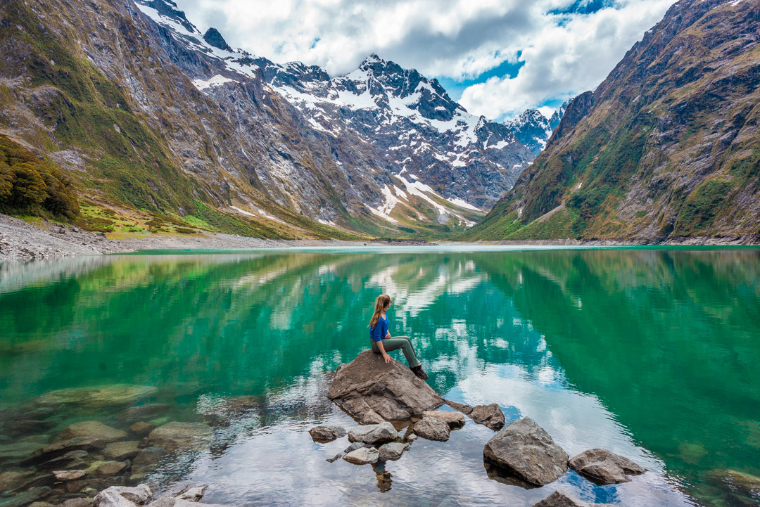 Lady sitting on a rock at Lake Marian in Fiordland National Park, New Zealand