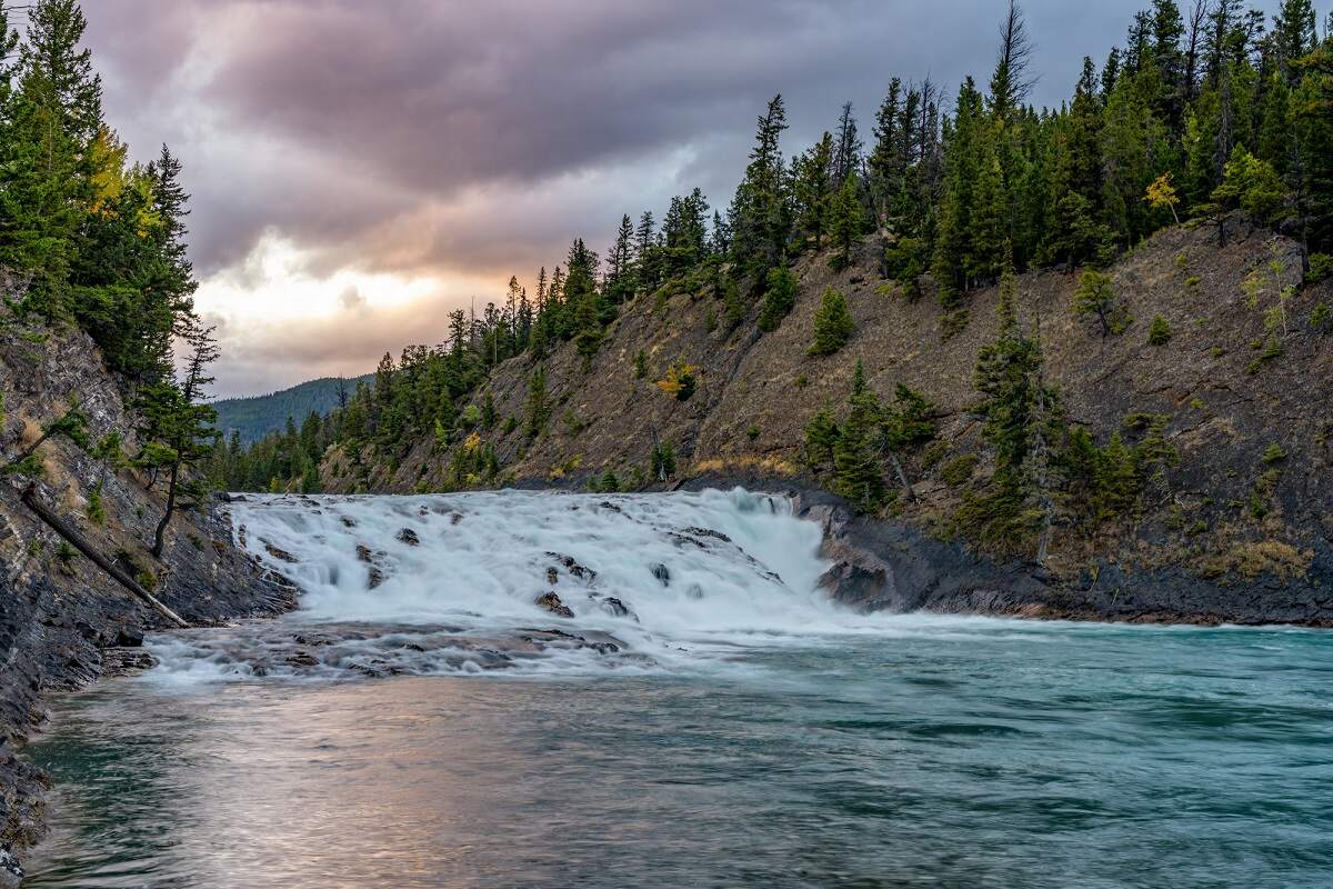 view of Bow Falls in Banff from the river's edge during sunset