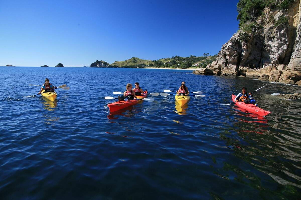 group of people kayaking to Cathedral Cove in the ocean with cliffs in the background
