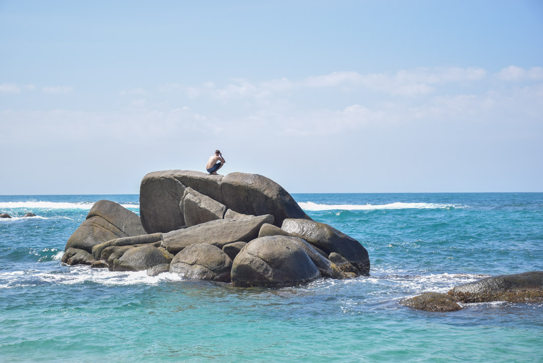 A man sits on a rock in the ocean at Cabo San juan Beach.
