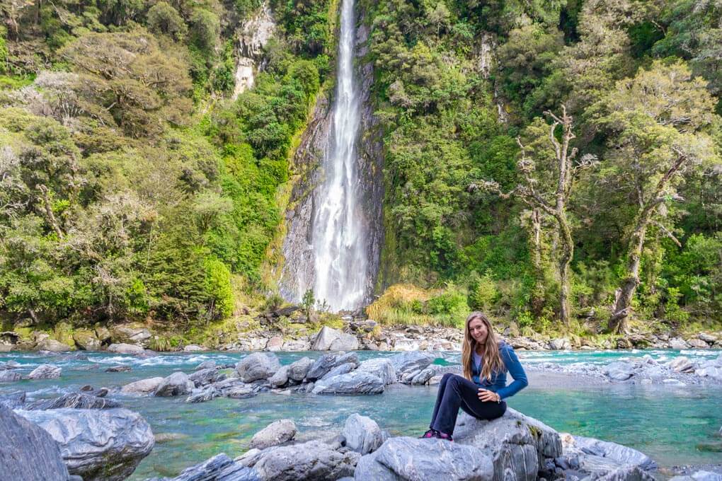 bailey sits on a rock in front of thunder creek falls, new zealand