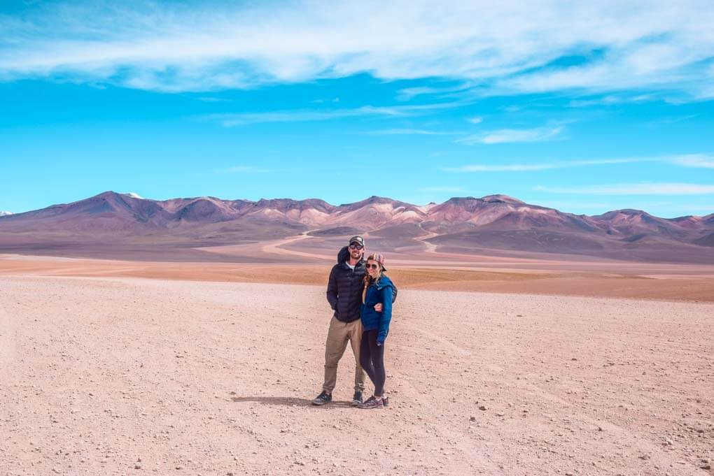 Bailey and Daniel pose for a photo on a desert area of the salt flats in Bolivia