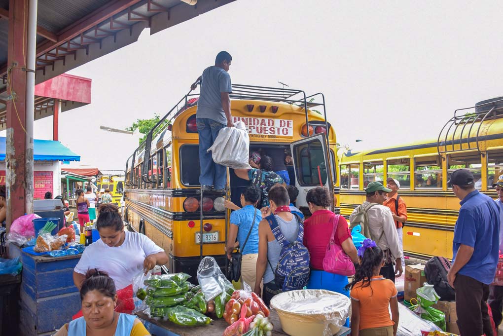 A bunch of people loading up te back of a chicken bus in Central America