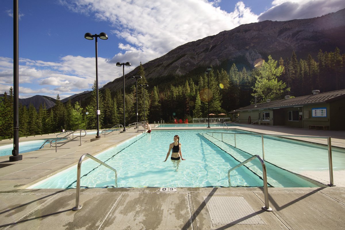 woman stands in the miette hot springs with mountains behind her