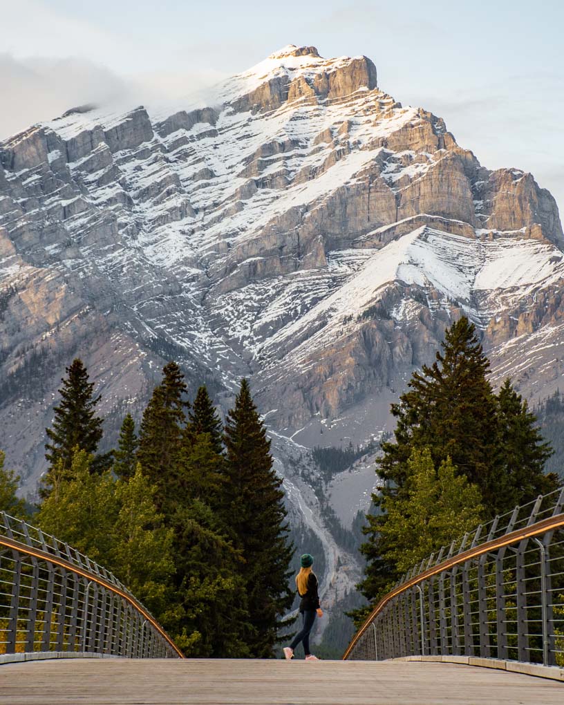 A lady walks along the Banff Pedestrian Bridge taking a photo for Instagram