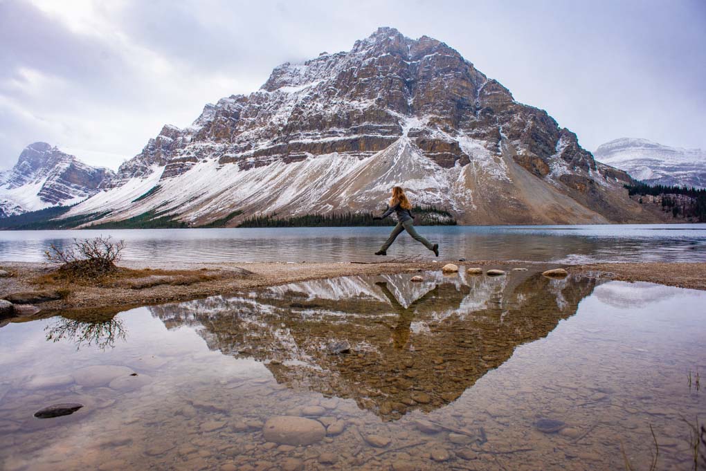 A lady jumps from rock to rock on the edge of the Bow Lake in Banff National Park