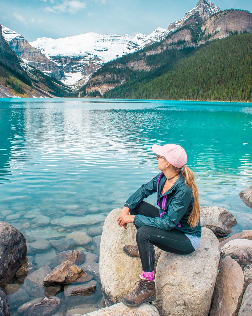 A lady sits on a rock at Lake Louise looking out over the water at the glacier and mountains