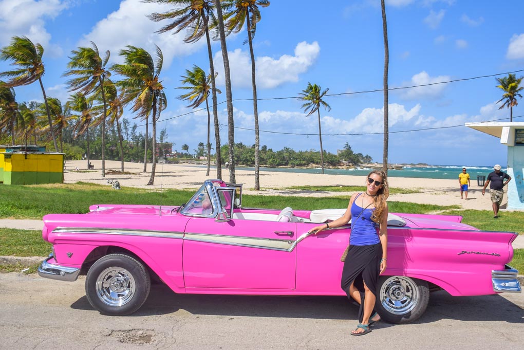 A lady poses with a vintage car at Playa del Este, Havana