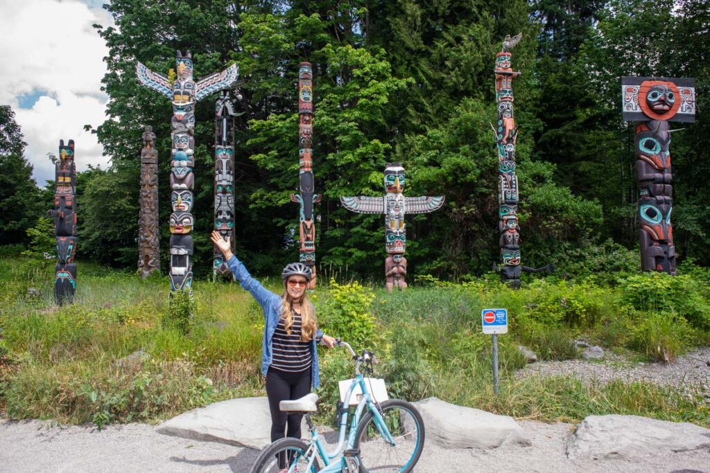 A lady poses for a photo in front of the Stanley Park Totem Poles