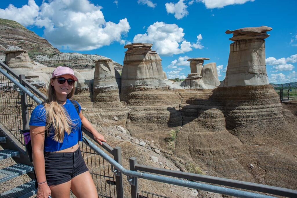 Bailey from Destinationless Travel poses with a hoodoos in Drumheller