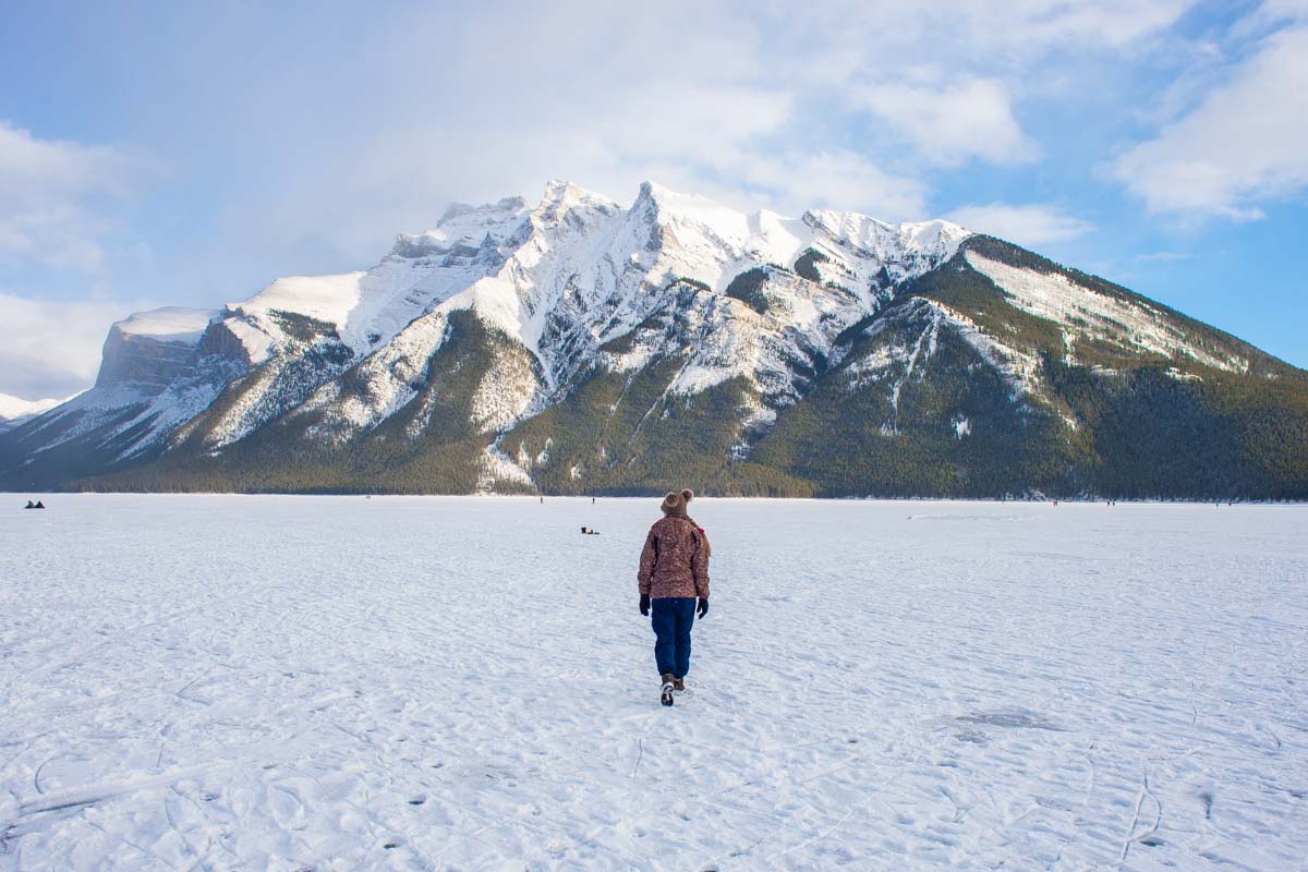 A lady walk's along a frozen Lake Minnewanka in Banff