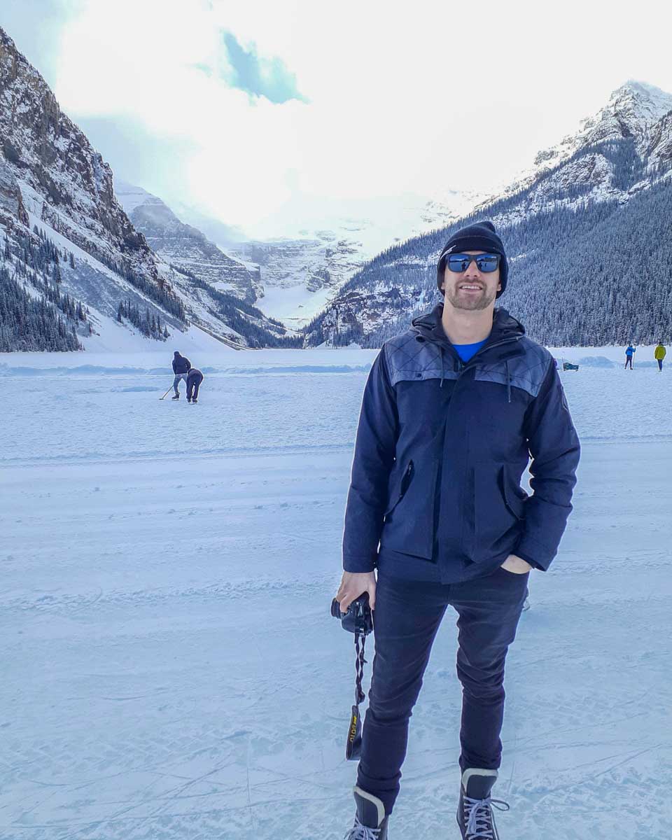 Daniel stands on frozen Lake Louise with mountains behind him
