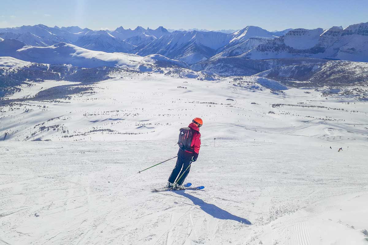 A man skies at the top of Sunshine Mountain Resort with tons of mountain peaks behind him