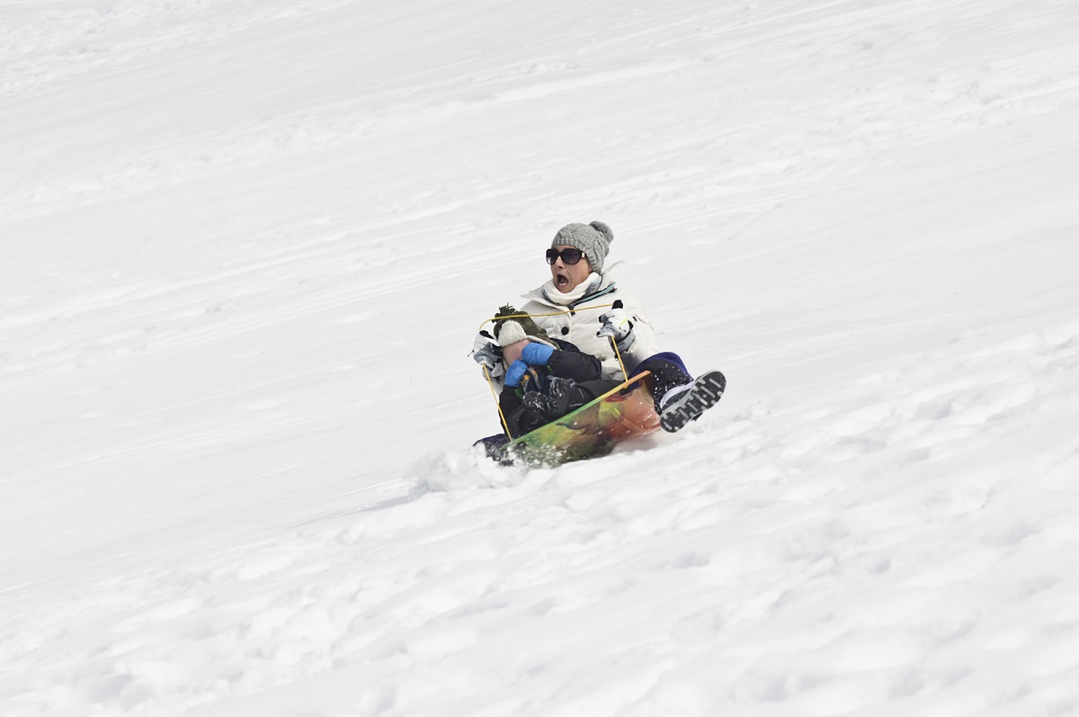 lady in a sled going down a hill of snow almost crashing with a scared look on her face