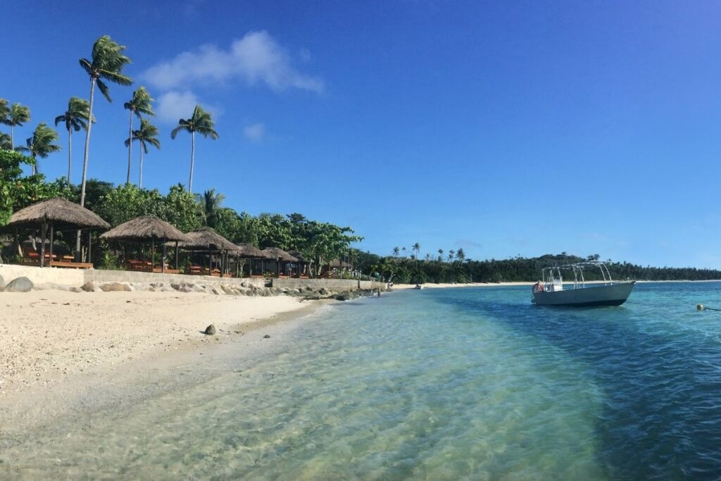 Yasawa Islands Resort beach area with tiki huts and a small boat on the bay.