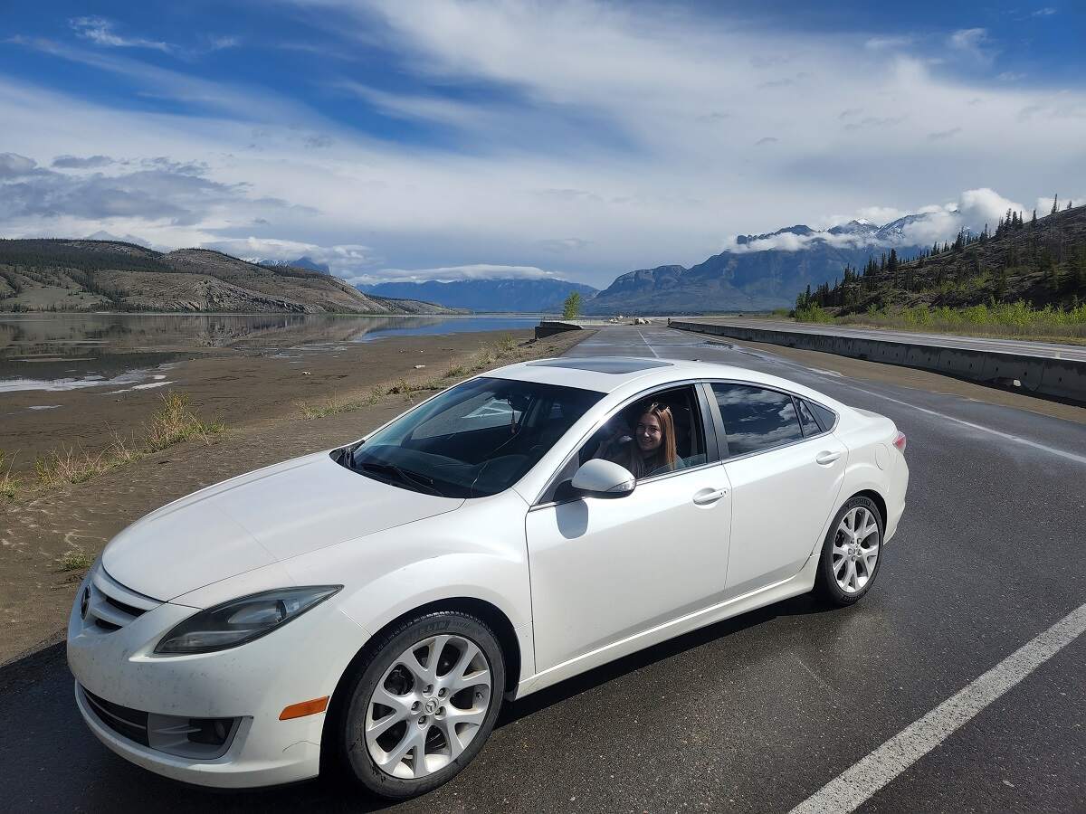 Bailey in a white car in Jasper National Park with mountains in the background.