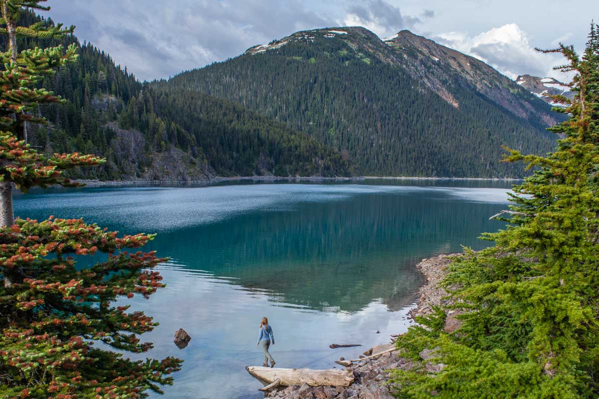 A lady stands on a rock on the edge of Garibaldi Lake in British Columbia, Canada on an overnight hike