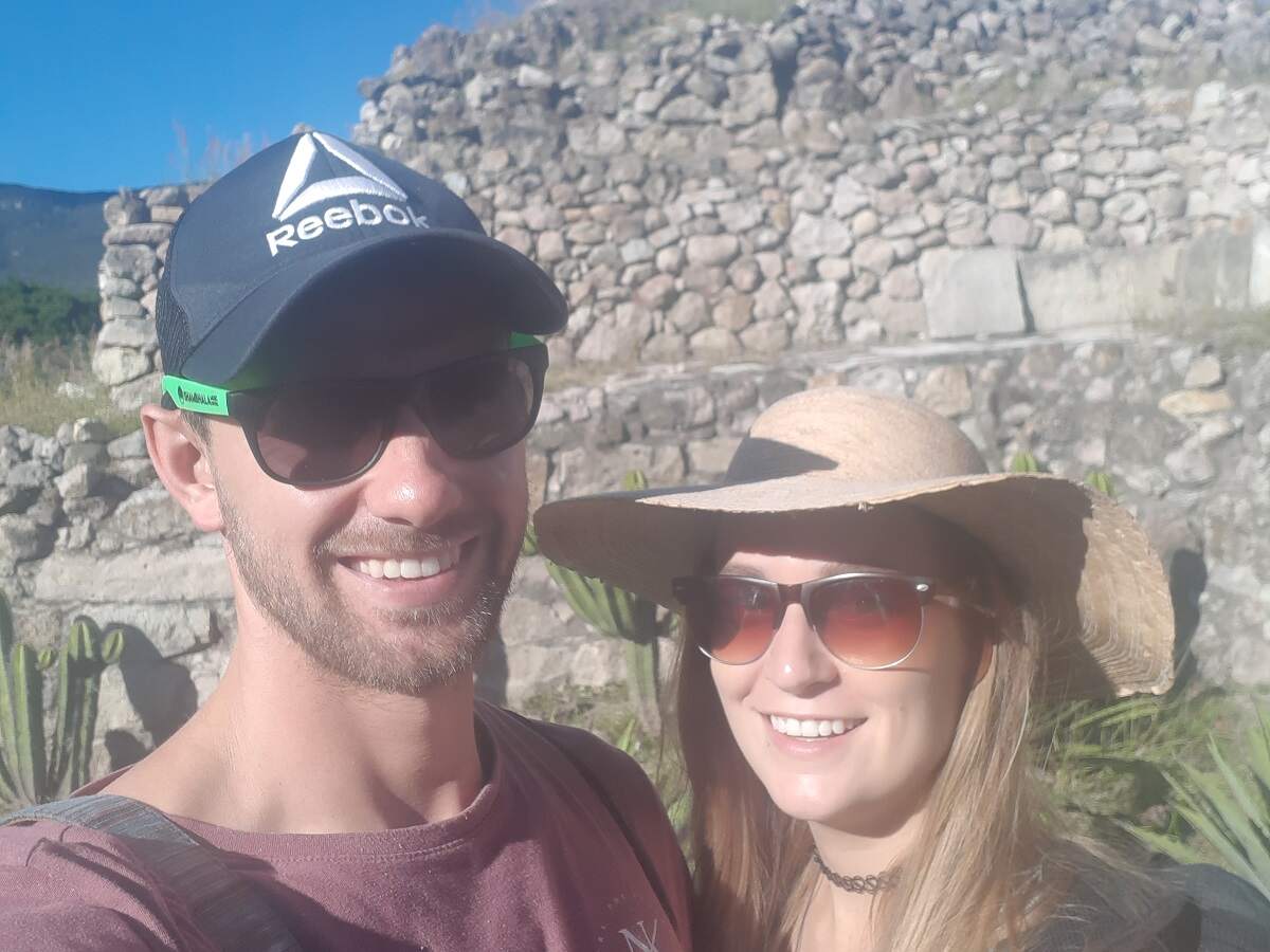 a mand and a woman take a selfie on a tour in Mitla from Oaxaca. Sunny day with ruins in the background.