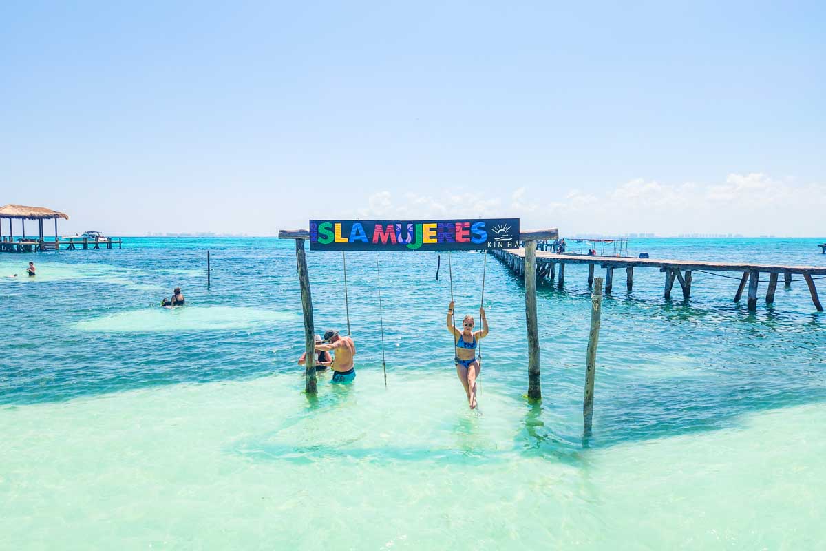 Bailey relaxes on a swing in the ocean with an Isla Mujeres sign about her on Isla Mujeres, Mexico