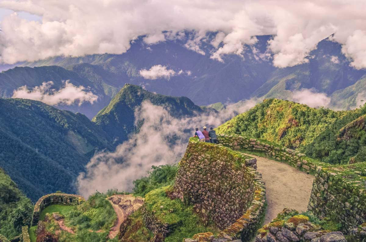 Three people stand overlooking phuyupatamarca on the Inca Trail near Cusco