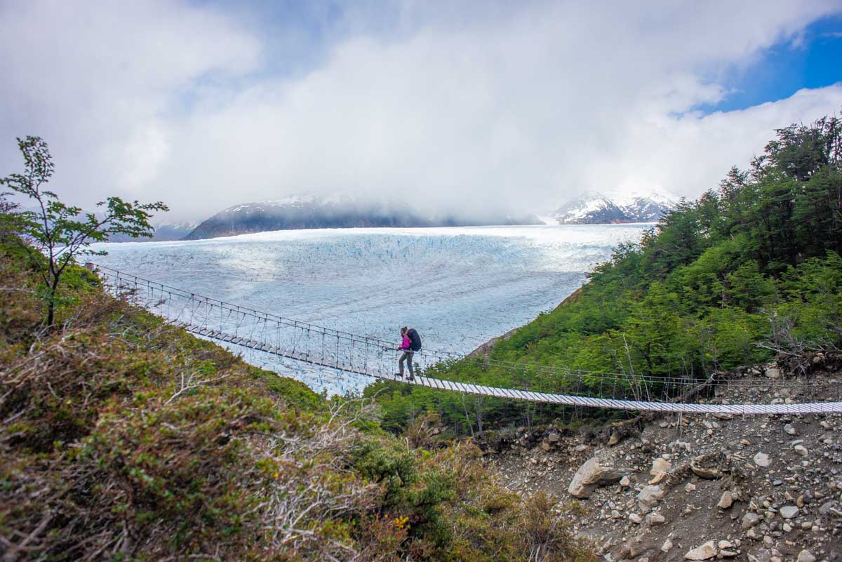 A lady walks a suspension bridge with Glacier Grey in the background