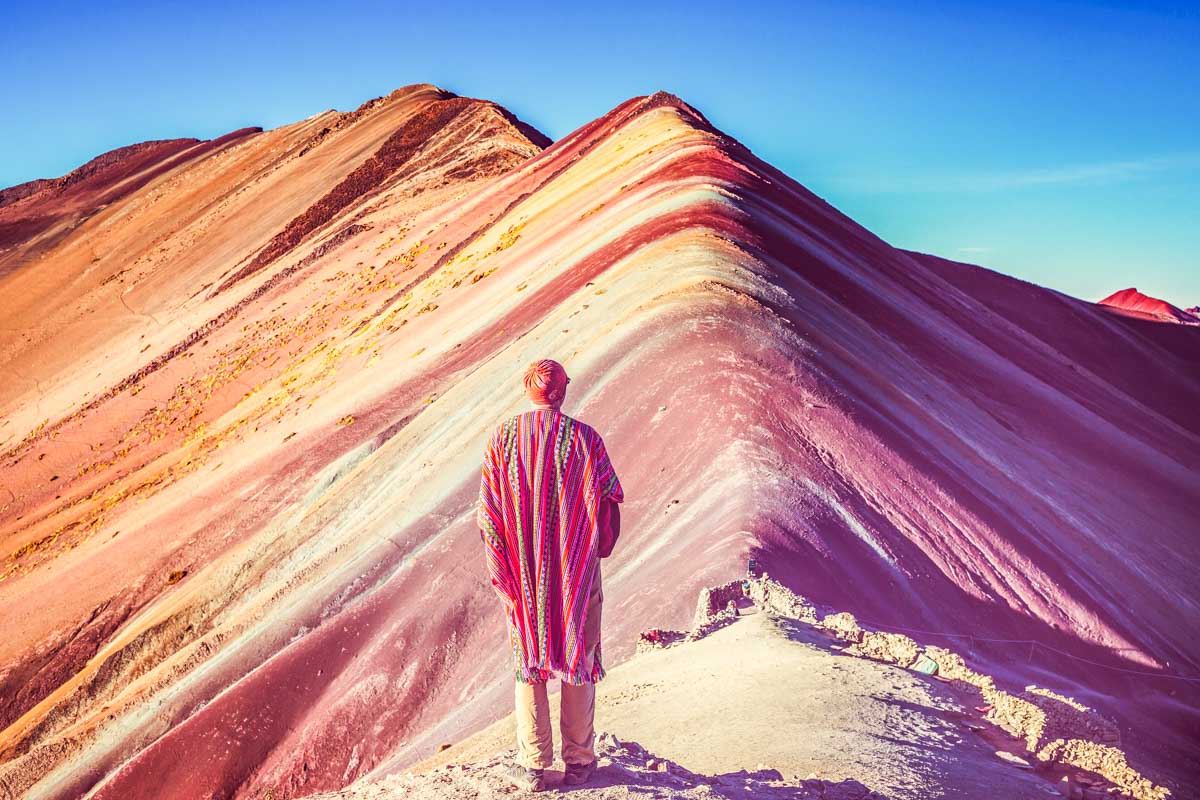 A man stands at the summit of Vinicunca or Rainbow Mountain
