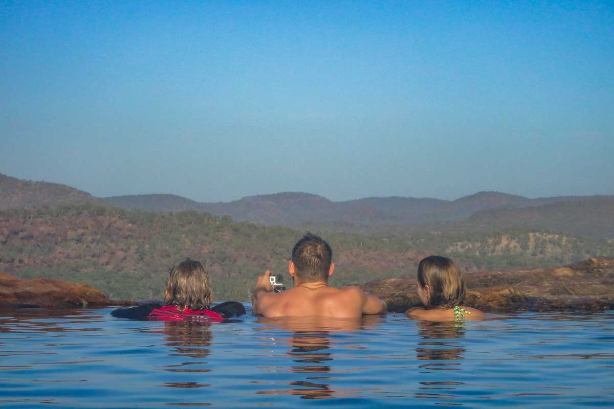 Three people sit in the infinity pool at gunlom falls in Kakadu National Park, Australia