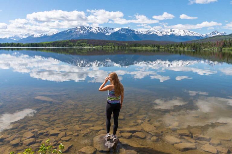 Bailey stands on the edge of the lake with stunning reflections at Pyramid Lake in Jasper National Park, Canada