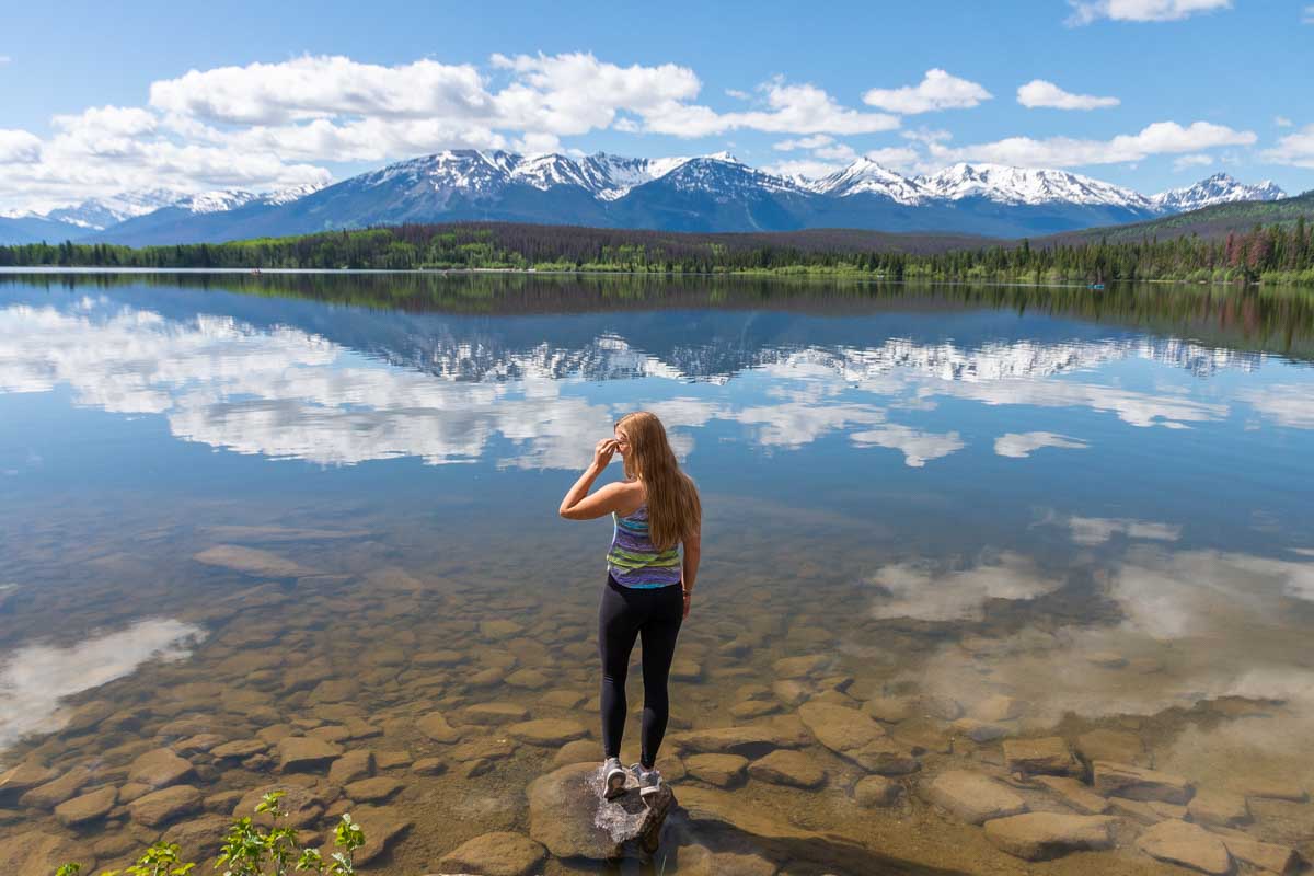 Bailey stands on the edge of the lake with stunning reflections at Pyramid Lake in Jasper National Park, Canada