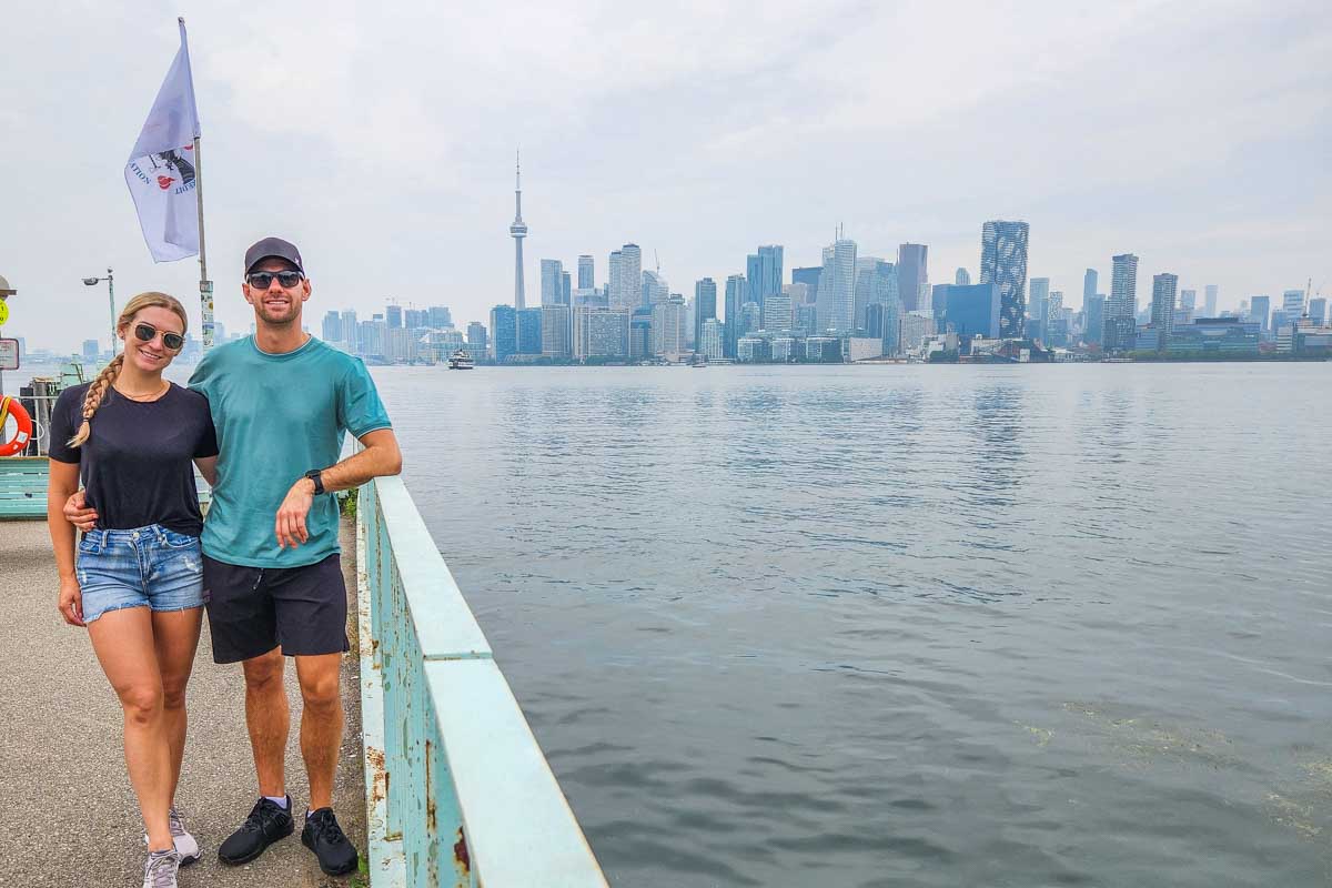 Bailey and Daniel pose for a photo at the ferry terminal on the Toronto Islands with a view of Torontos skyline in the background