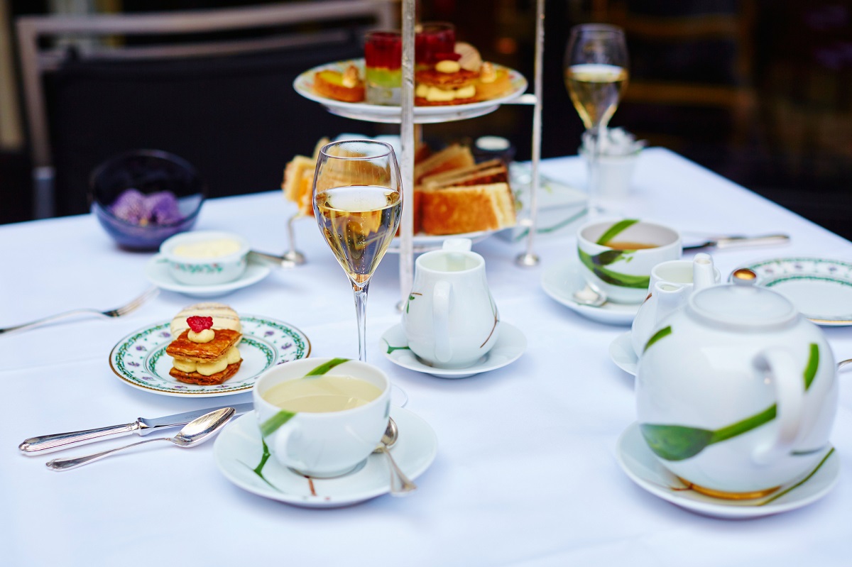 a white table with fancy teacups, champagne, and small finer foods and cakes