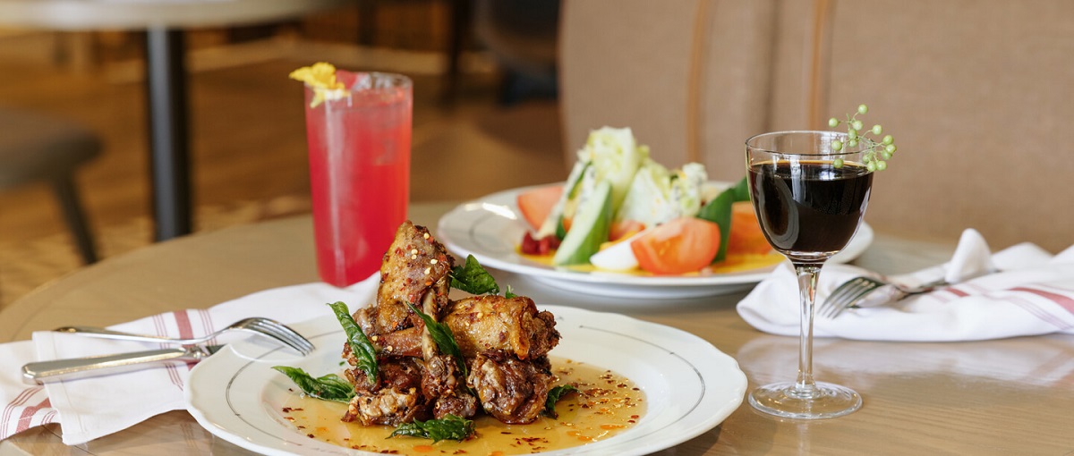 a plate of chicken wings with a bright pink cocktail behind it at Alpine Social 