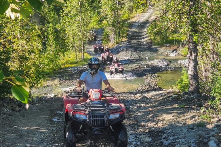 People ride an ATV through a puddle on a tour in Whistler, BC