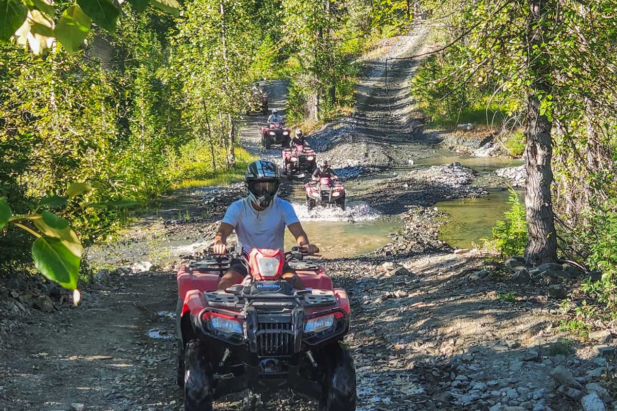 People ride an ATV through a puddle on a tour in Whistler, BC