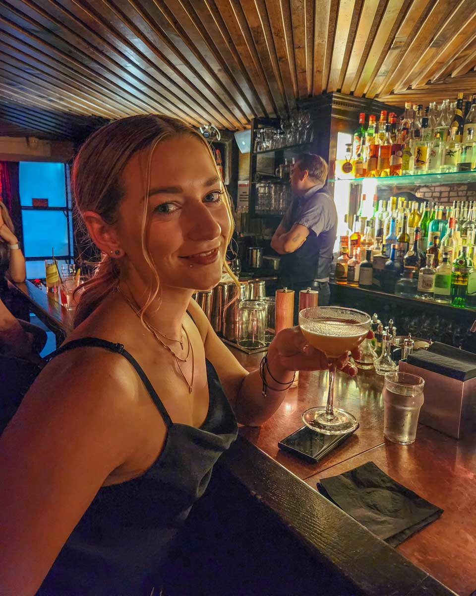 Bailey sips a cocktail at Please Don't Tell in New York City, NY