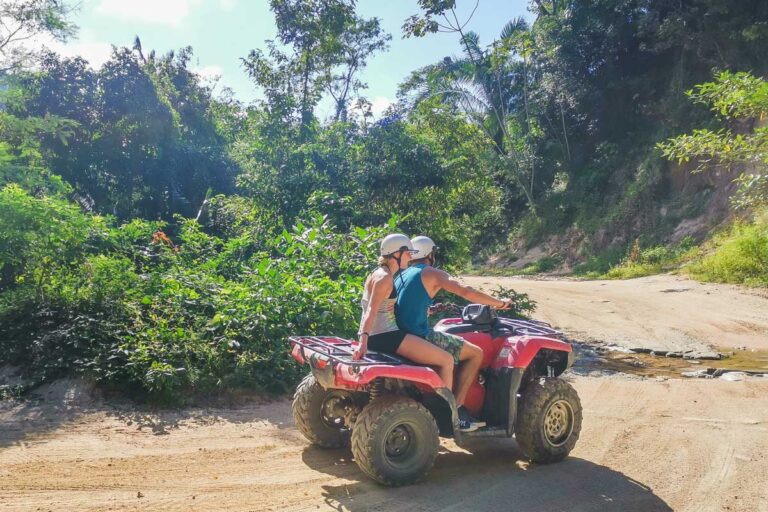 Two people ride an ATV around a corner in Tulum, Mexico