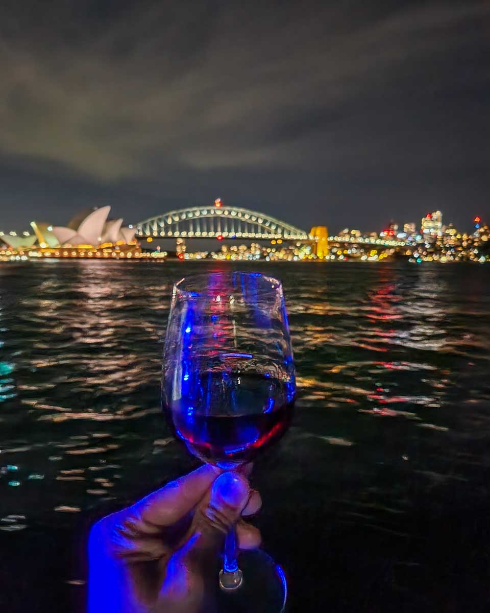 A glass of wine on a dinner cruise with views in the background of Sydney harbour Bridge and Sydney Opera House