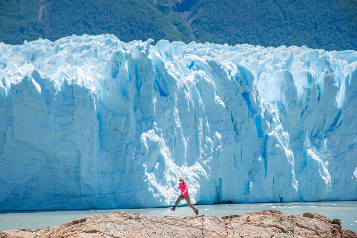 A lady jumps between rocks with Perito Moreno Glacier in the background