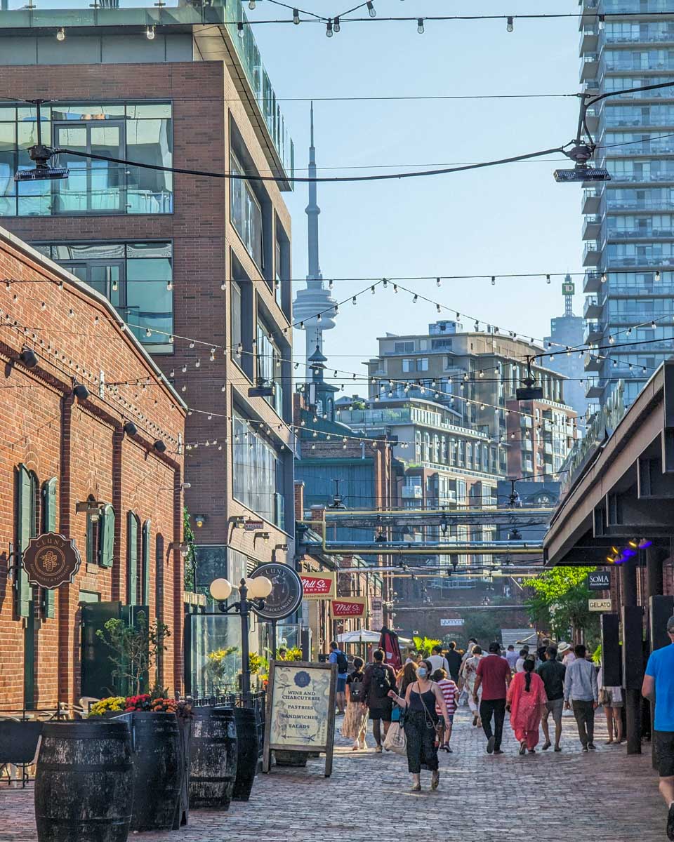 People walk through the Toronto Distillery District with the CN Tower in the background in Toronto, Canada