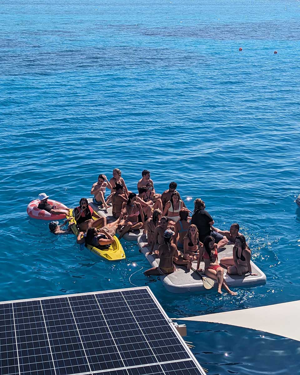 A group of people sit on a floating platform just off the Seventh Heaven Fiji Floating Platform