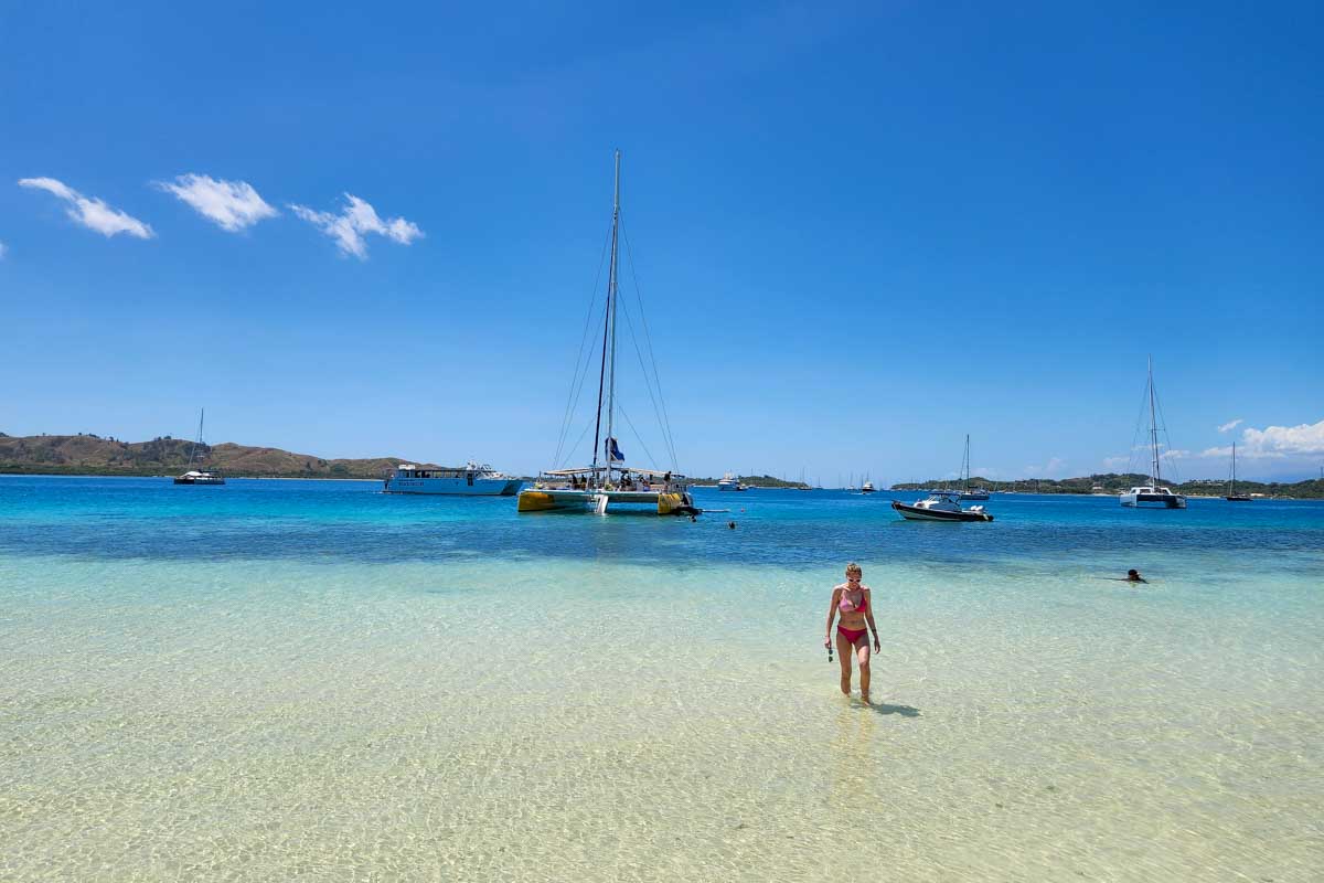 A woman walking up to the sand bar from the water with the Sabre catamaran behind her fiji