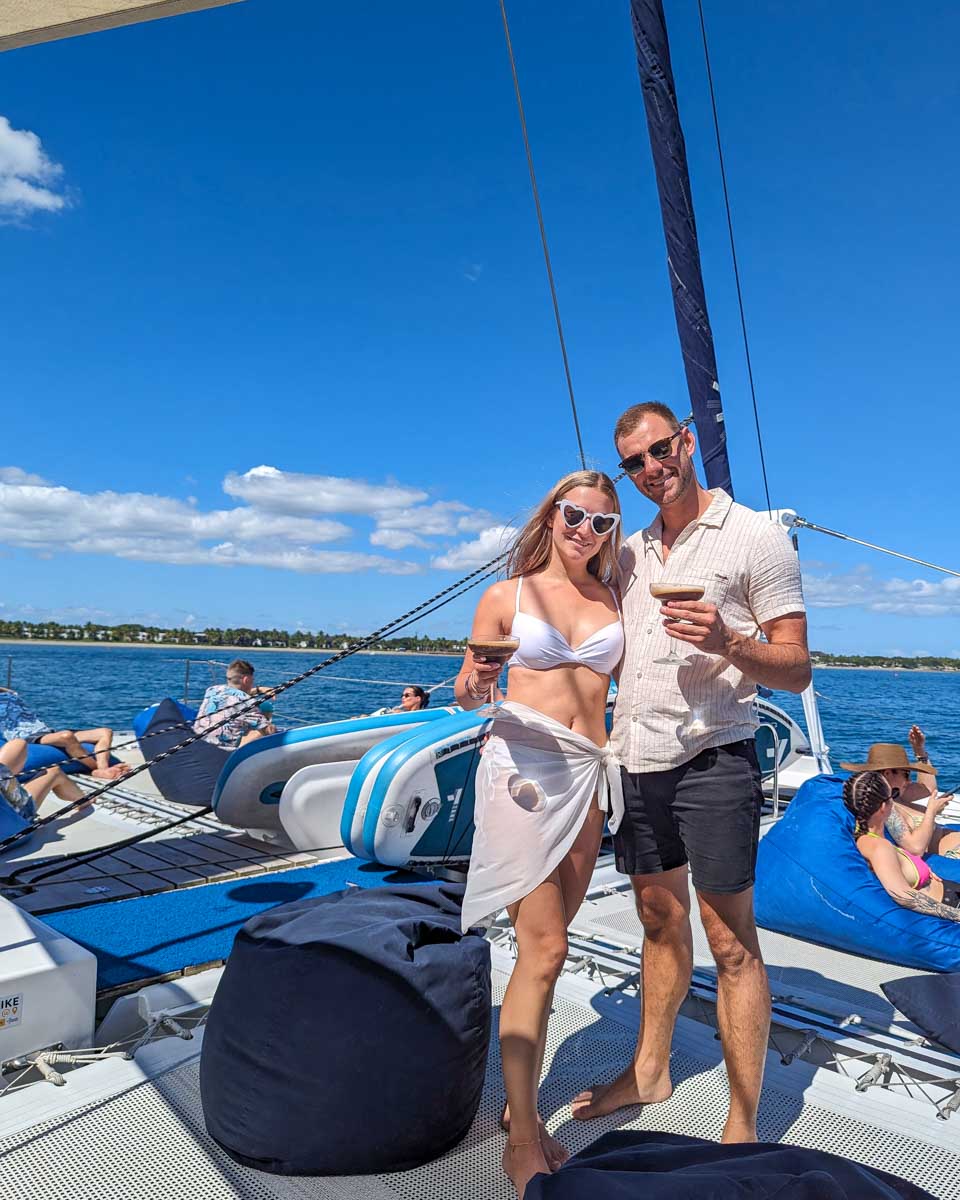 Bailey and Daniel on the deck of the sabre catamaran holding drinks and smiling fiji