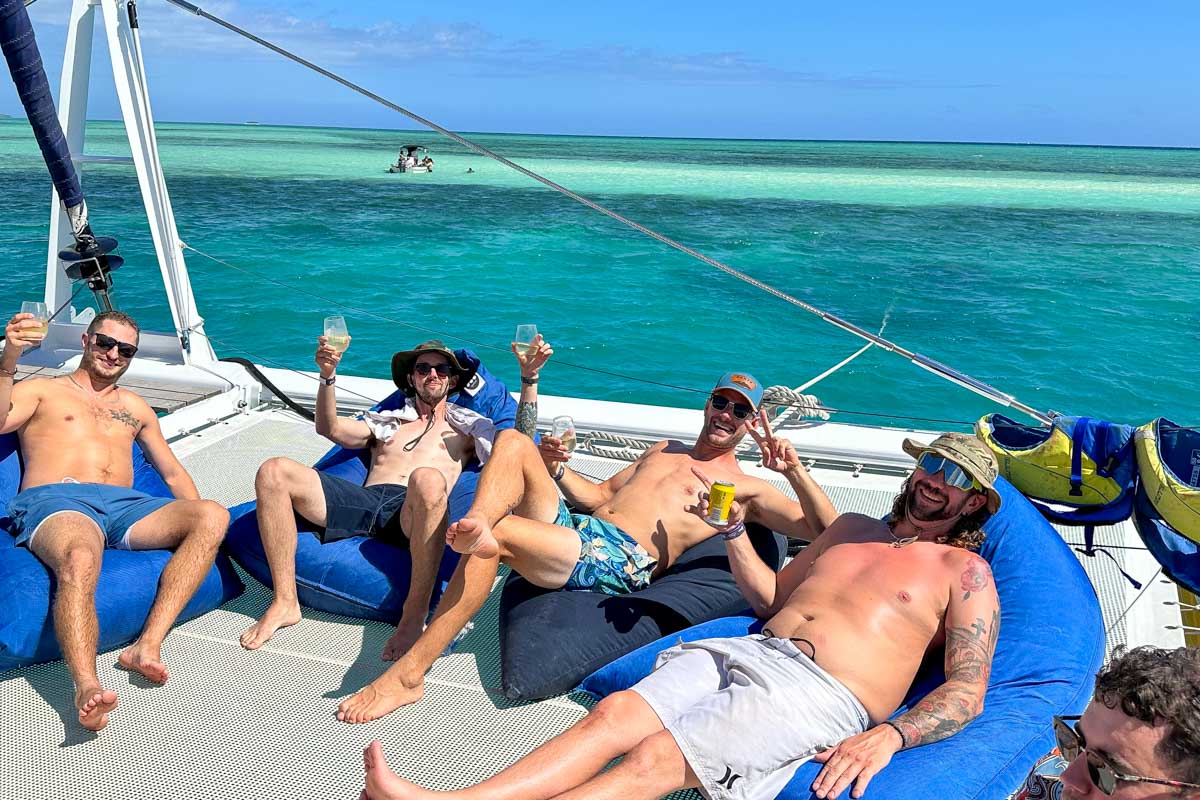 Daniel and friends on beanbag chairs raising their drinks and laughing aboard the sabre catamaran Fiji
