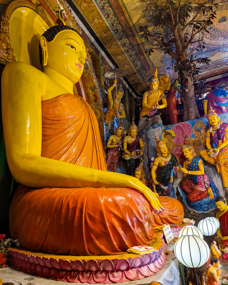 Looking at the large statue of the Buddha up close with other paintings in the background at the Gangarama temple Sri Lanka, Colombo