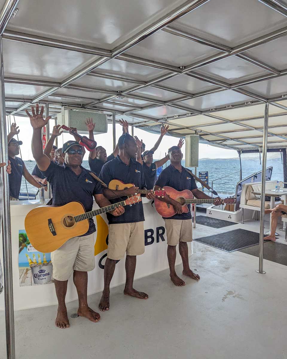 The crew of the sabre catamaran with guitars singing and waving as they perform fiji